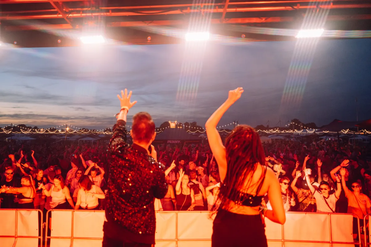 Deejay Plus beim Festival mit DJ und tanzender Menge.